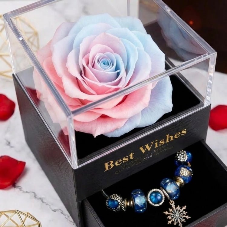 Angled close-up of a pastel two-tone pink and blue preserved rose in a clear case with a charm bracelet in the open drawer.