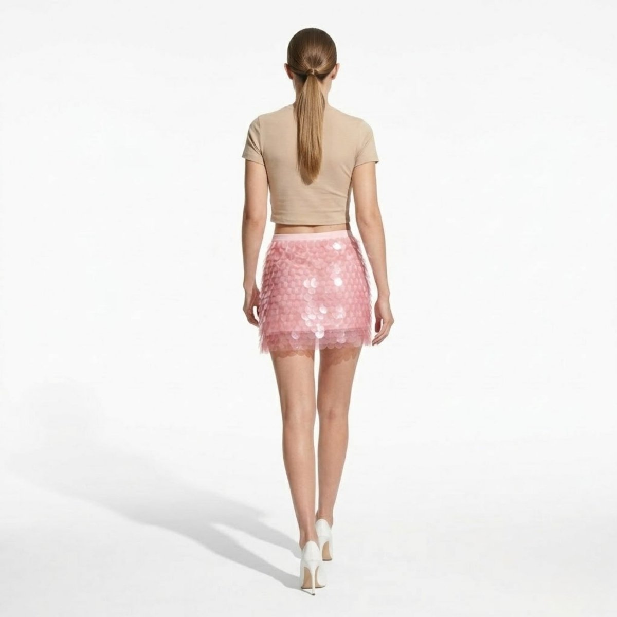 Back view of a high-waisted pink sequin skirt showing the layered disc texture, banded waist, and flattering mini length.