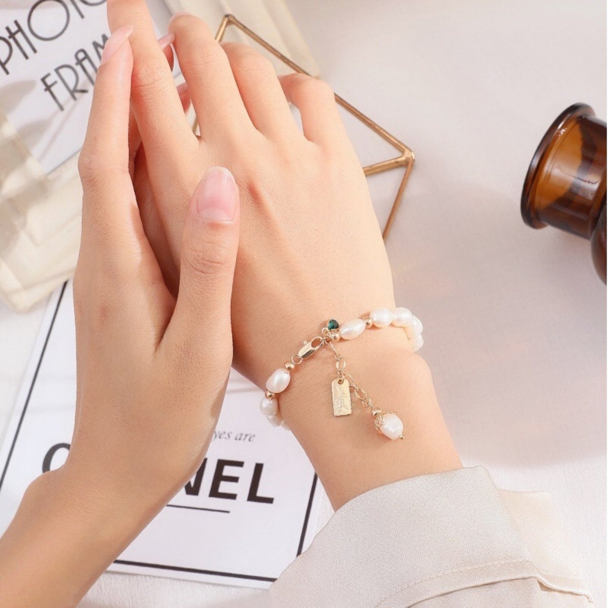 A close-up view of the Nathalia pearl bracelet's 18k gold plated lobster clasp, emerald charm, and custom tag.