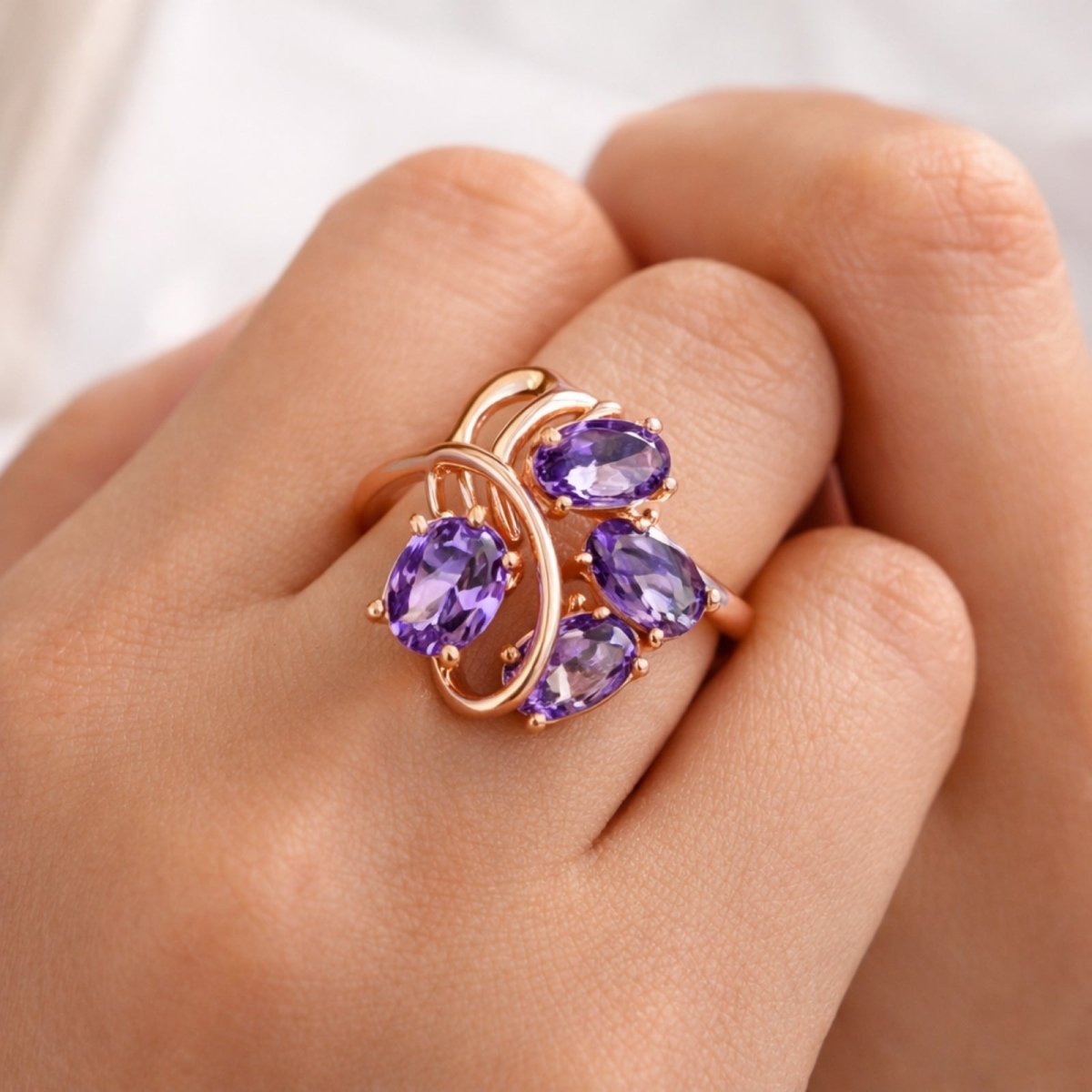 Close-up view of the 14k rose gold Kouvr Annika ring with four purple zircons on a woman's finger, highlighting the intricate design details.