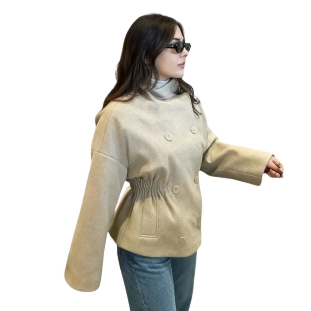 Side view of a model in the Kouvr beige wool jacket with a defined cinched waist, wearing sunglasses and walking.