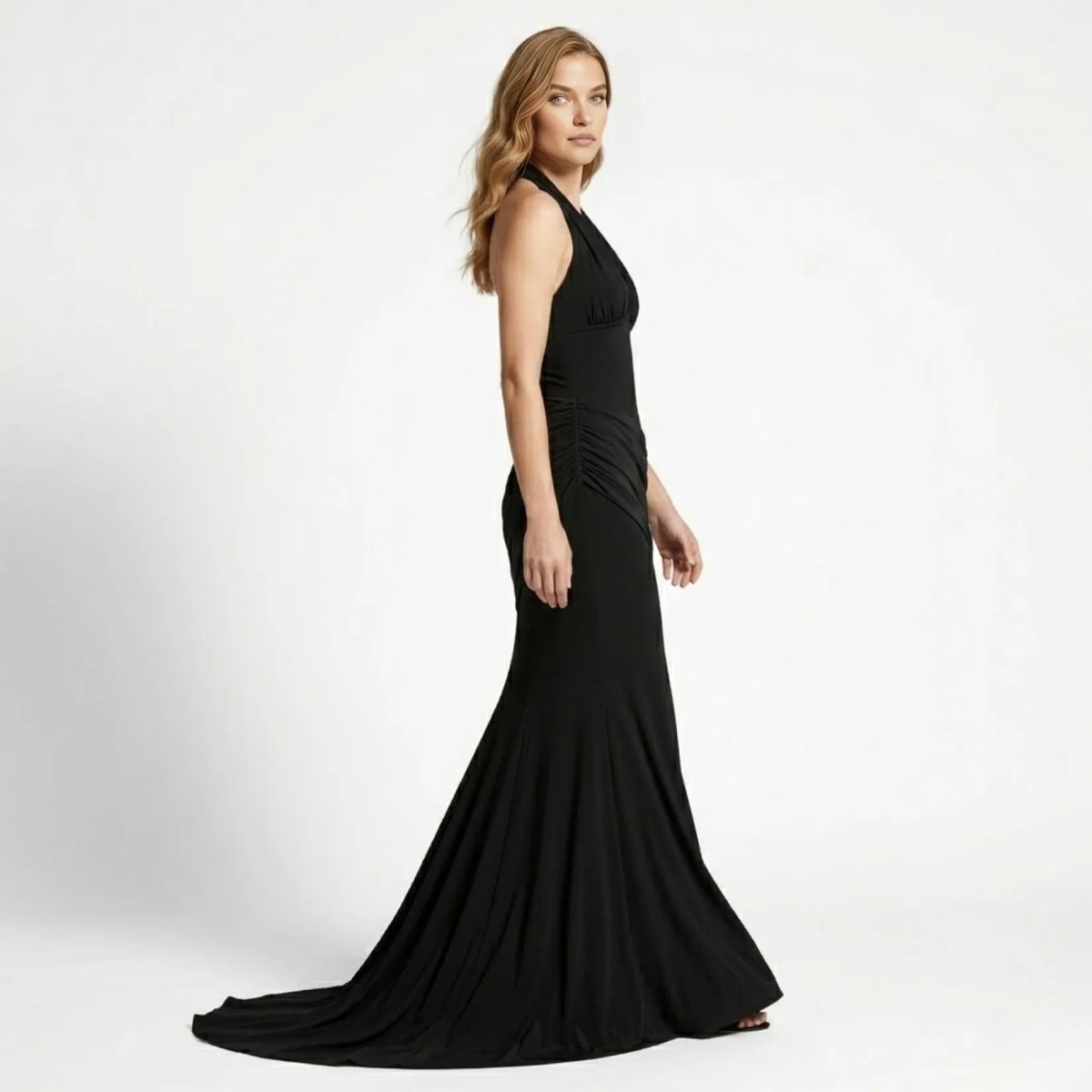 Side profile view of a glamorous black form-fitting mermaid evening gown highlighting asymmetrical draped hip details by Kouvr.