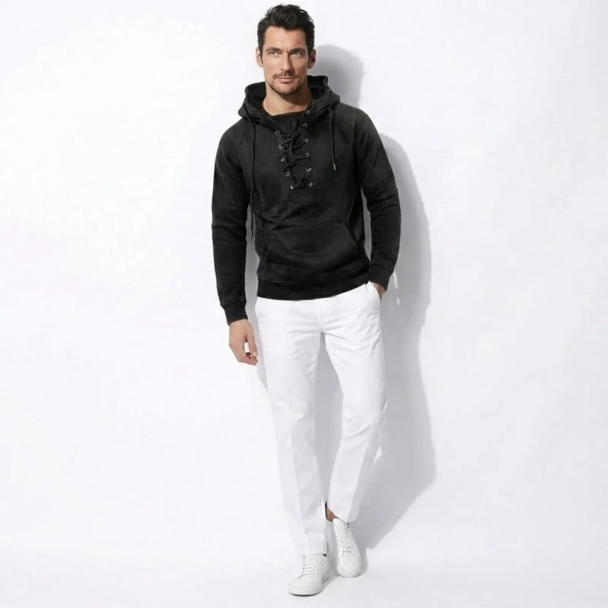 Male model wearing the Kouvr Cannon washed black lace-up hoodie with white trousers and sneakers, standing against a white background.