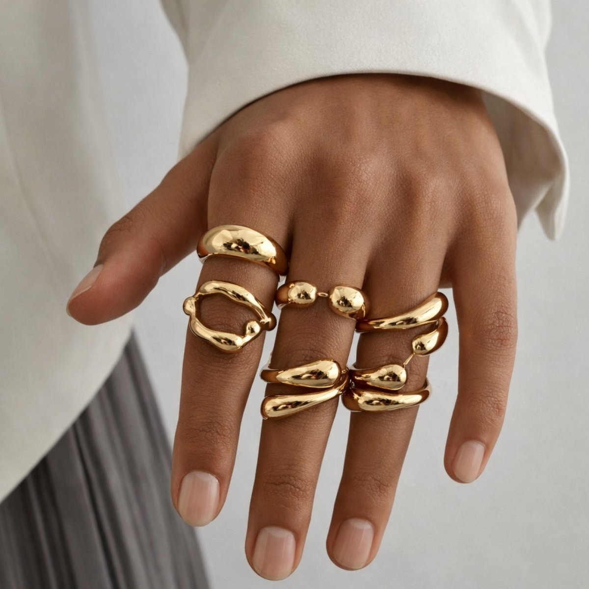 Detailed close-up of a hand wearing the complete Kouvr gold ring set, highlighting the various dome, wrap, and sculptural designs on each finger.