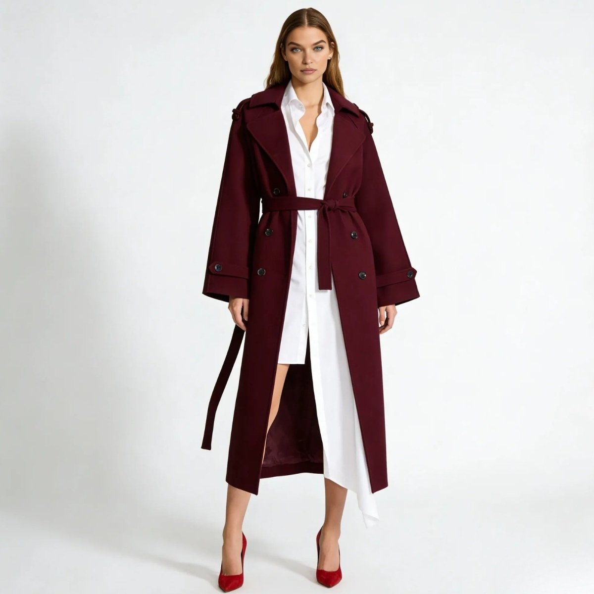 A female model wearing the Esther long burgundy wool trench coat from Kouvr Fashion, shown from the front with the belt tied over a white shirtdress.