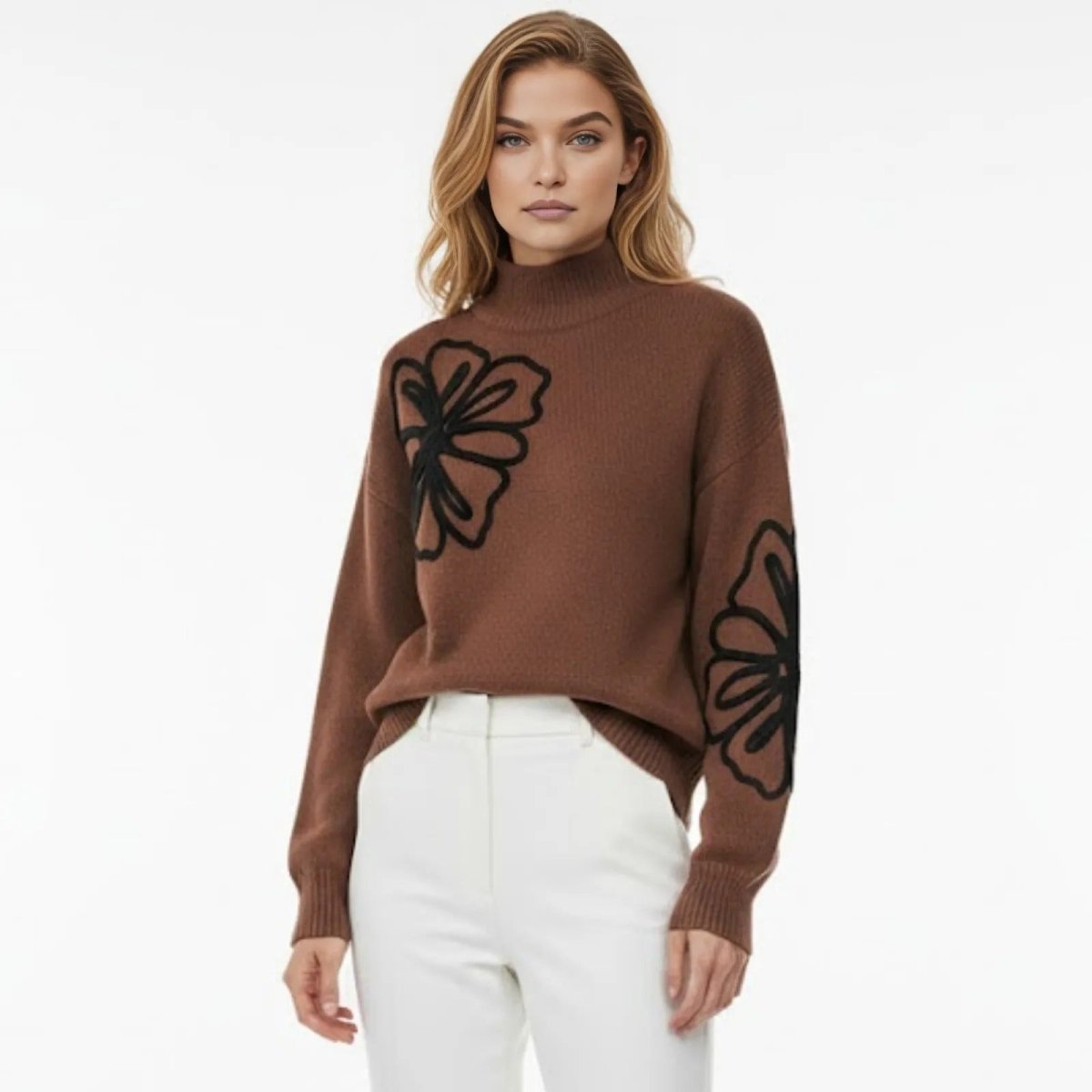 Model facing forward wearing the Kouvr Fashion brown mock neck sweater with large black floral embroidery, styled with high-waisted white trousers.
