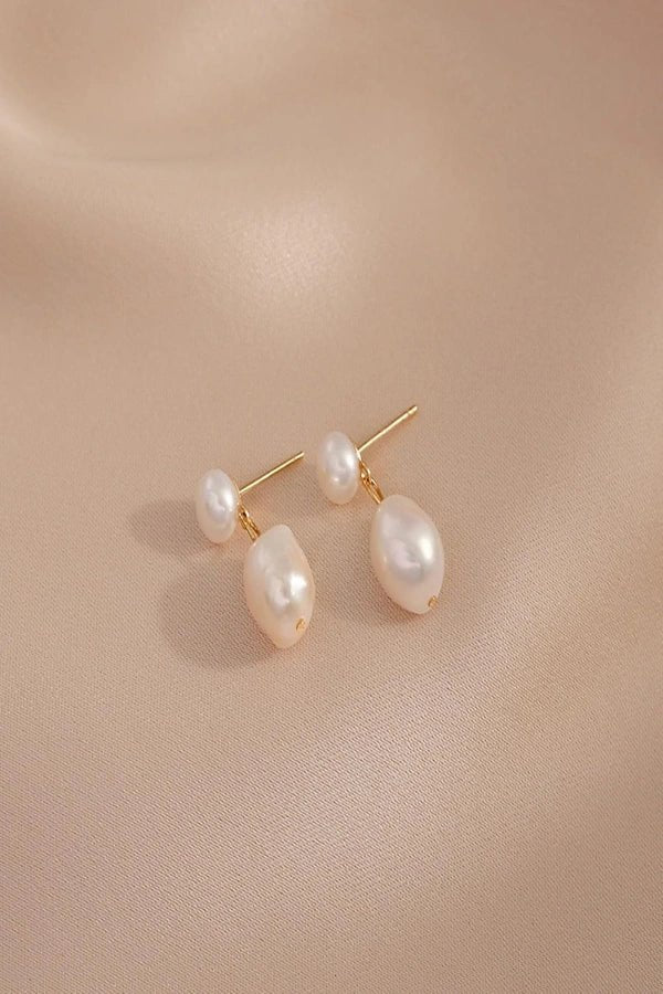 Pearl Kouvr earrings on a beige fabric background
