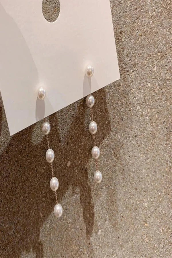 Pearl Kouvr earrings on a white card against a textured beige background