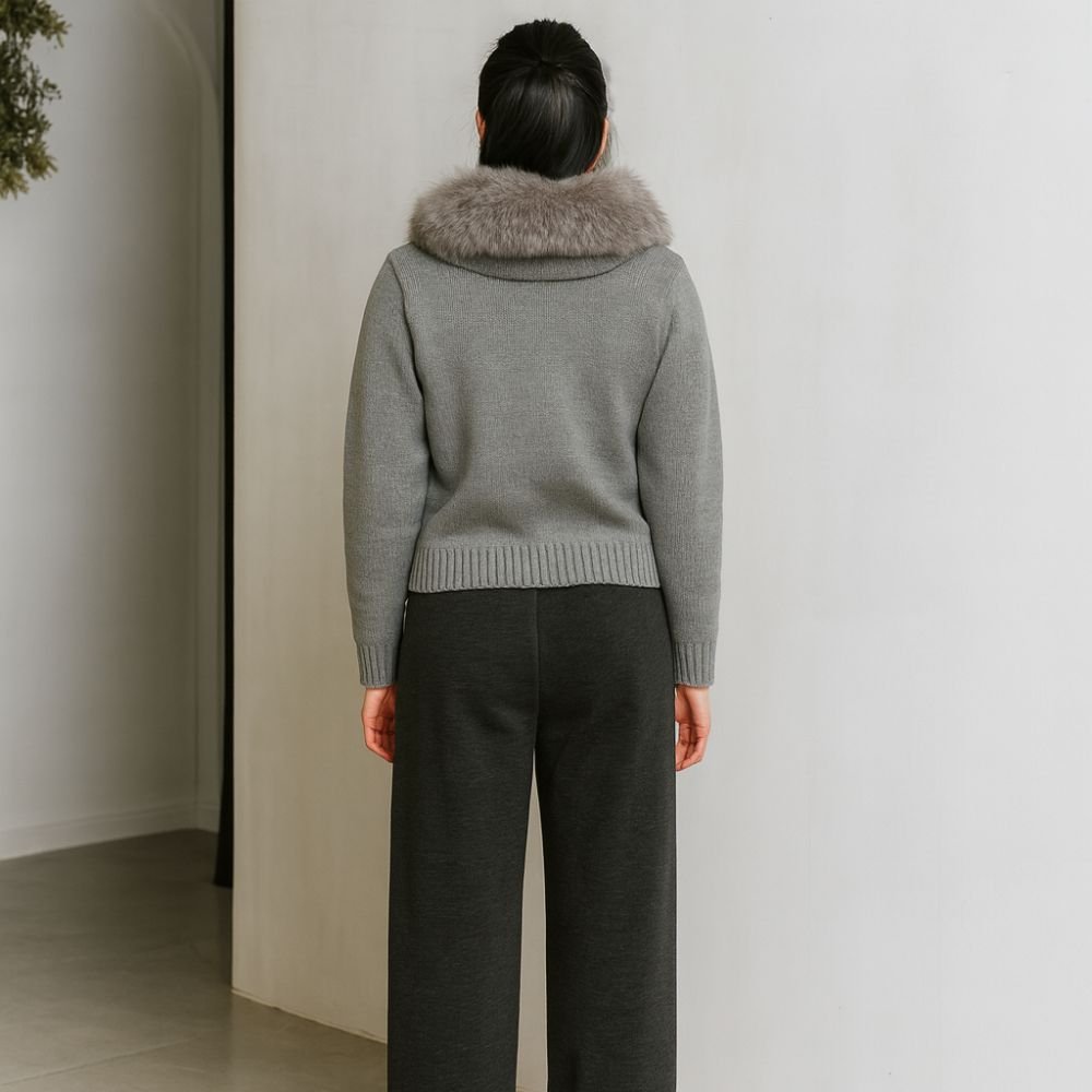 Person wearing a gray kouvr sweater with a fur collar against a plain wall.
