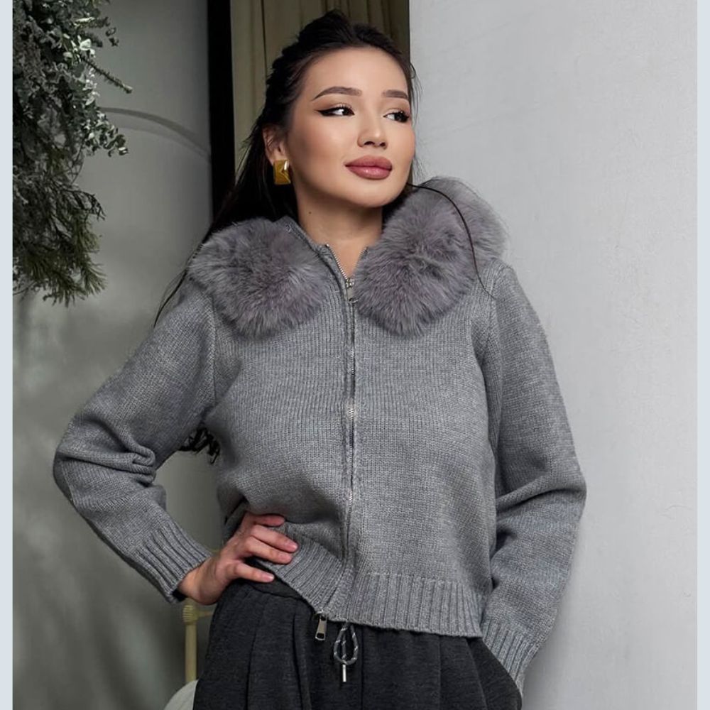 Woman wearing a gray kouvr sweater with a fur collar indoors.