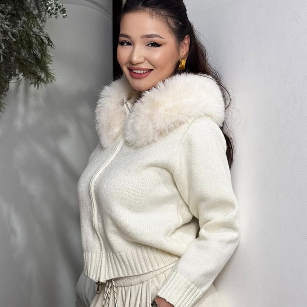 Woman wearing a ivory kouvr sweater with a fur collar against a snowy background