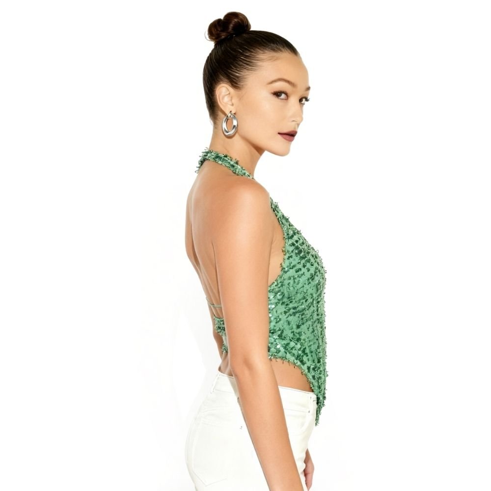 Woman wearing a kouvr green textured top with white pants on a white background