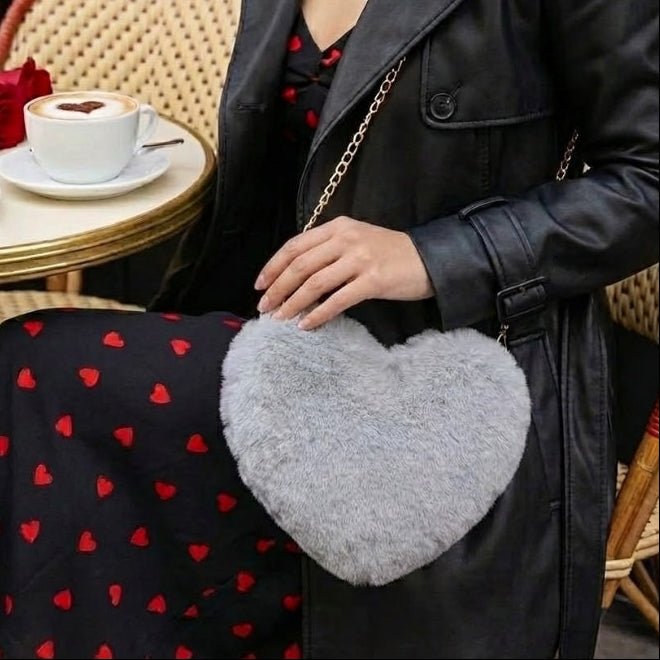 Model sitting at a Parisian cafe wearing a black leather jacket and heart-print dress, holding the grey faux fur Kouvr Fashion heart-shaped crossbody bag.
