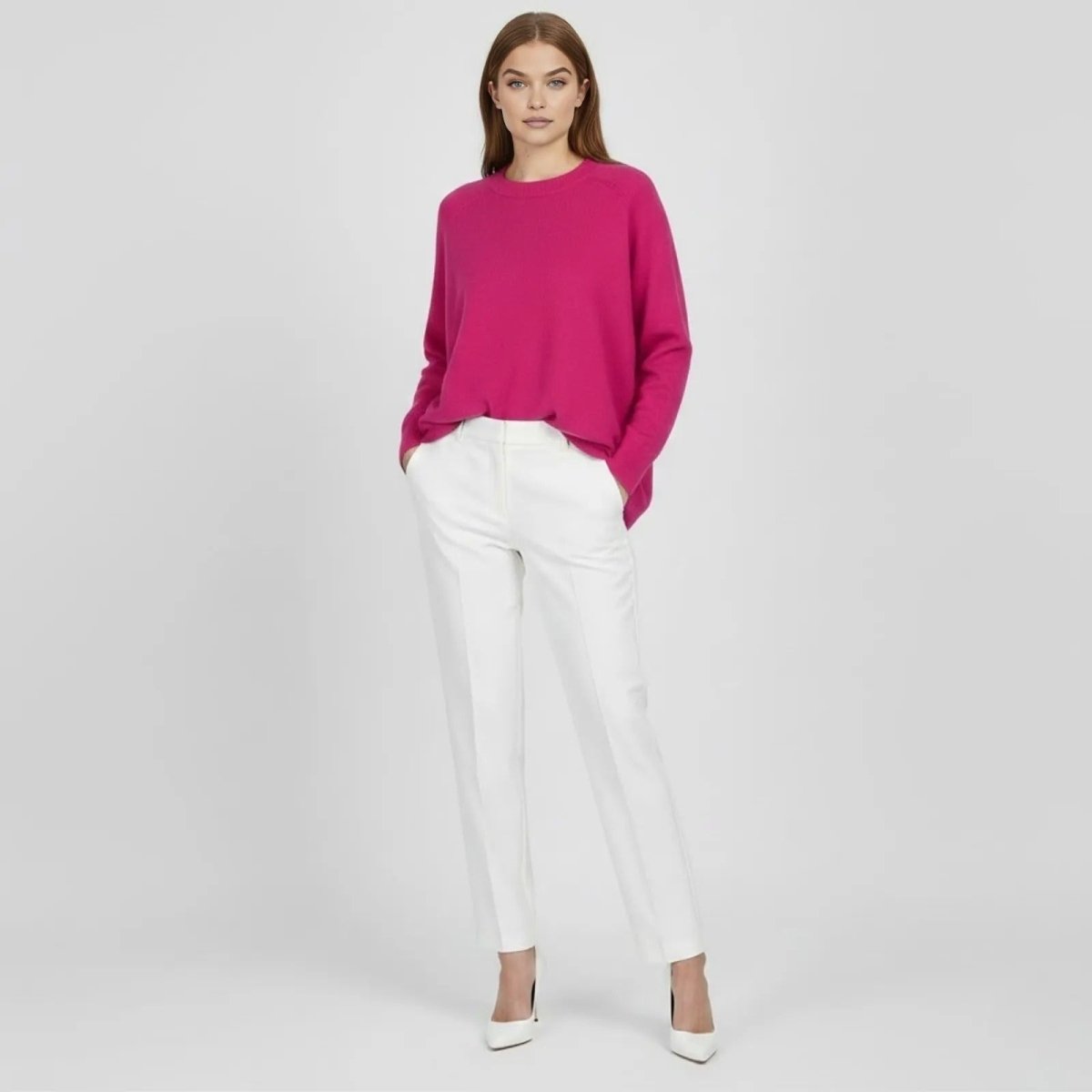 Model wearing the Kouvr Fashion oversized cashmere wool sweater in fuschia pink, styled with white trousers and white heels, viewed from the front.
