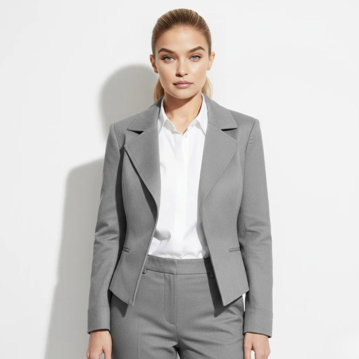 Woman wearing The Maddie tailored grey blazer from Kouvr Fashion, shown from the front with a white shirt and matching trousers.