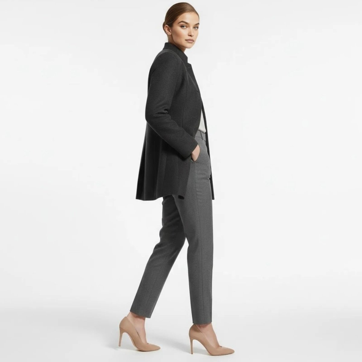 Side profile of a model walking in the Kouvr A-line funnel neck coat in dark grey, showcasing its elegant silhouette, structure, and mid-thigh length.