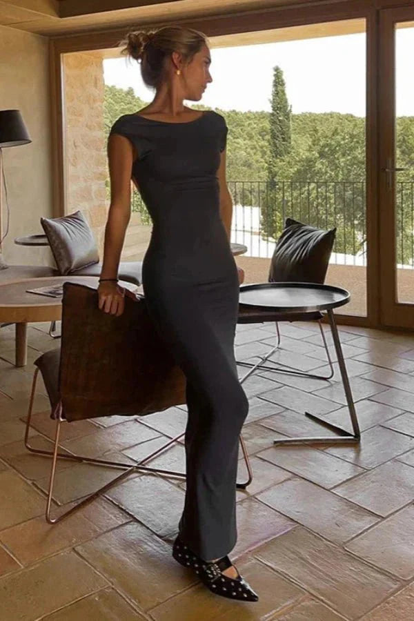 Model wearing the Kouvr Grace black boat neck maxi dress with a full view of the open back