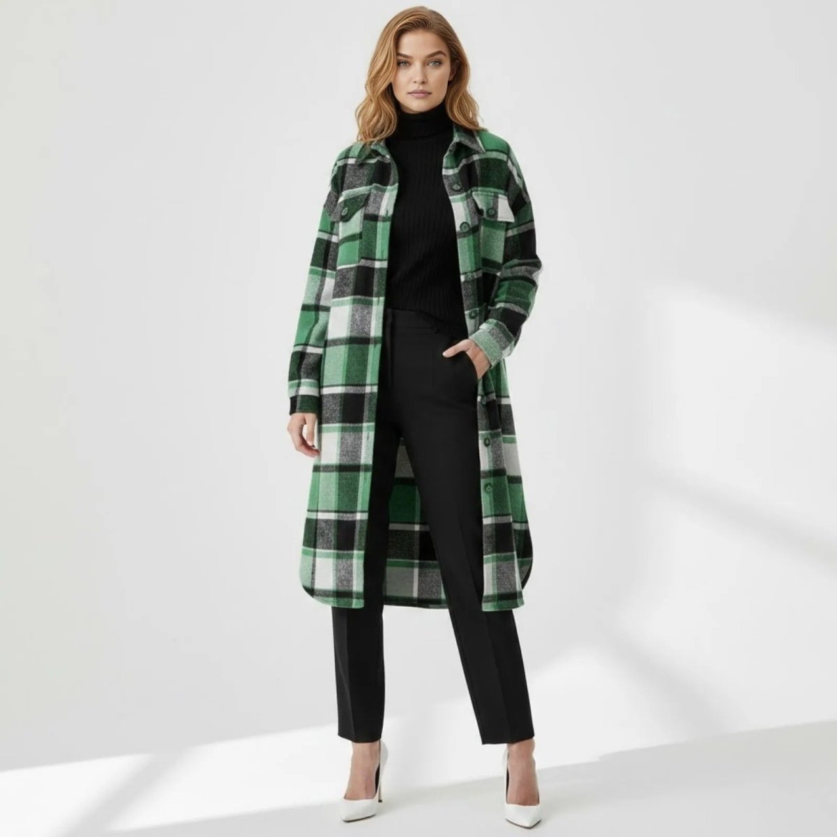 Model wearing the Kouvr green and black plaid longline shacket open over a black turtleneck and trousers, standing forward in a studio.