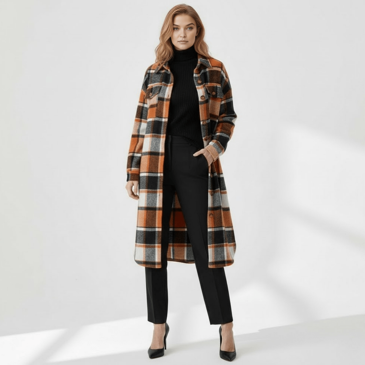Woman wearing the Kouvr Janet Longline Plaid Shacket in orange and black, styled with a black turtleneck and trousers, facing forward.