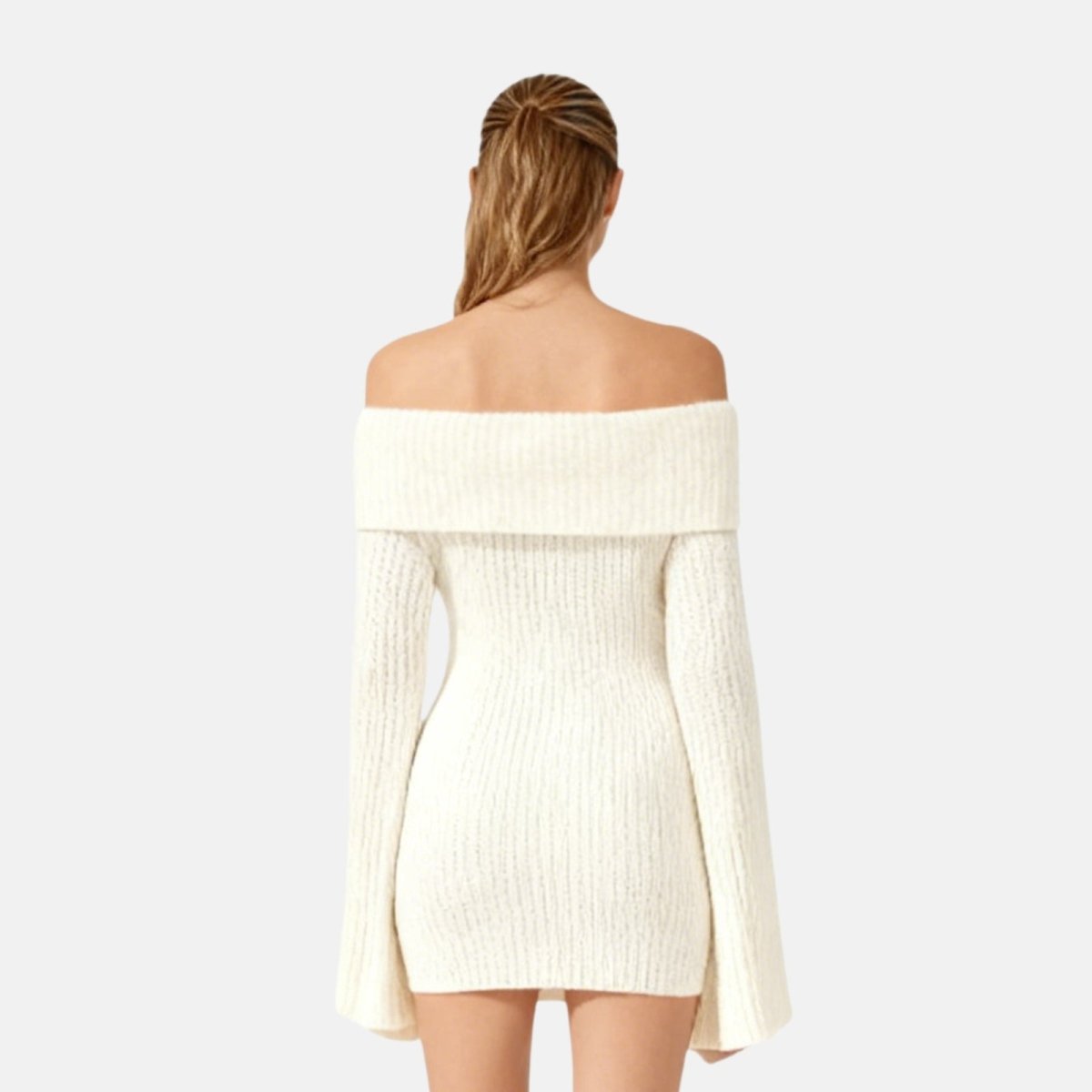 Woman wearing a ivory off-shoulder sweater dress against a light gray background