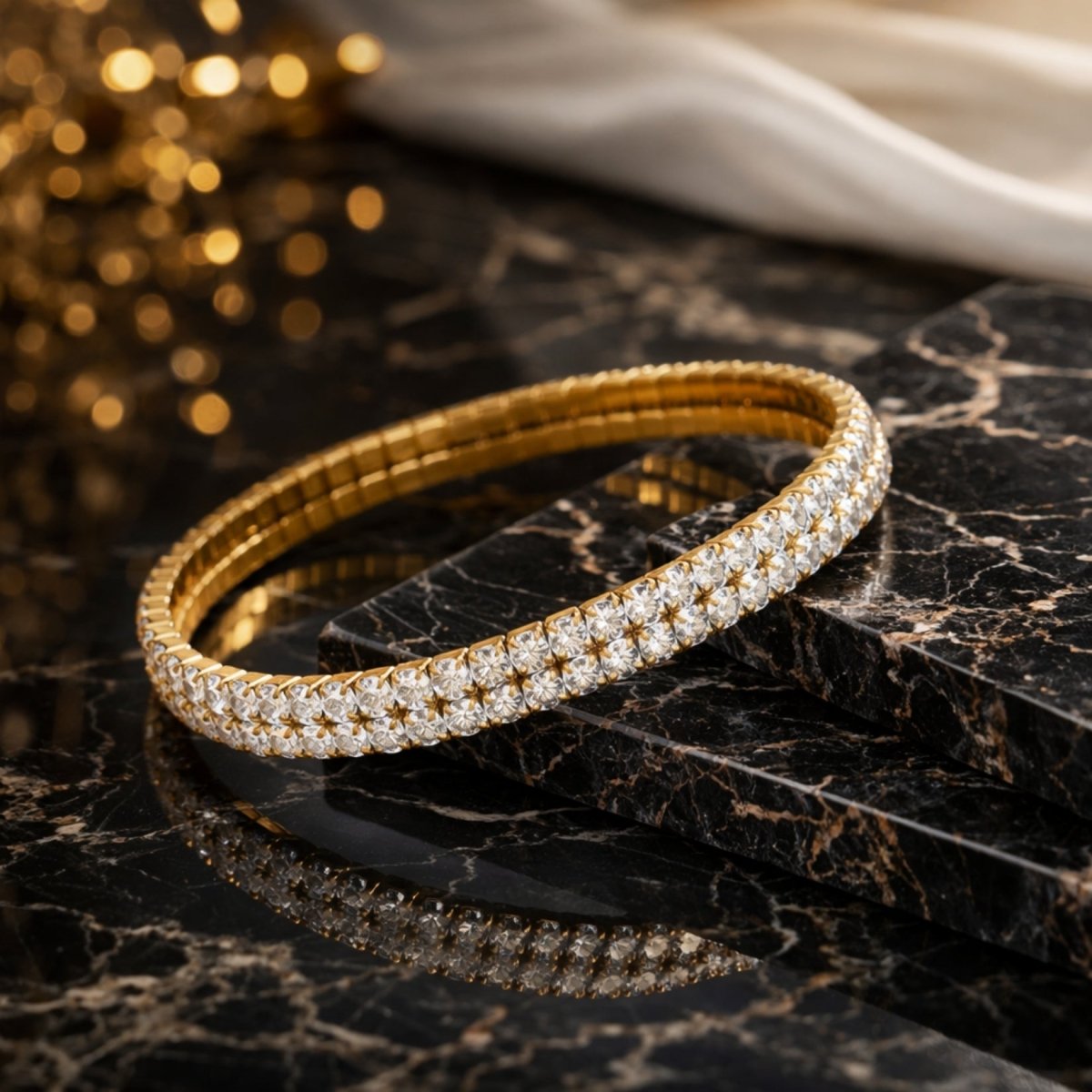 The Kouvr Marzanna gold stretch tennis bracelet resting on a black marble surface with its reflection visible.