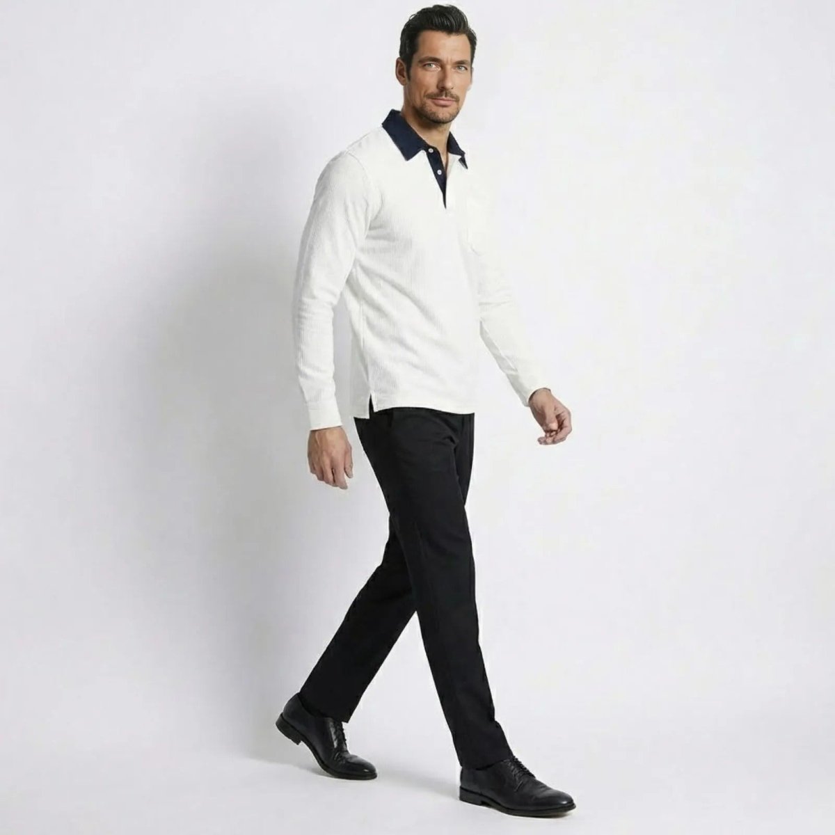 Model in a walking pose showing the side profile of the Kouvr men's white corduroy long sleeve polo shirt and its fit.