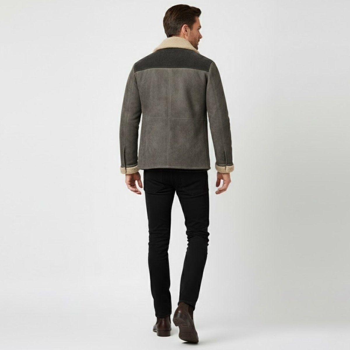 Back view of a male model wearing the Kouvr shearling jacket, highlighting the two-tone dark grey yoke panel and structured seaming.