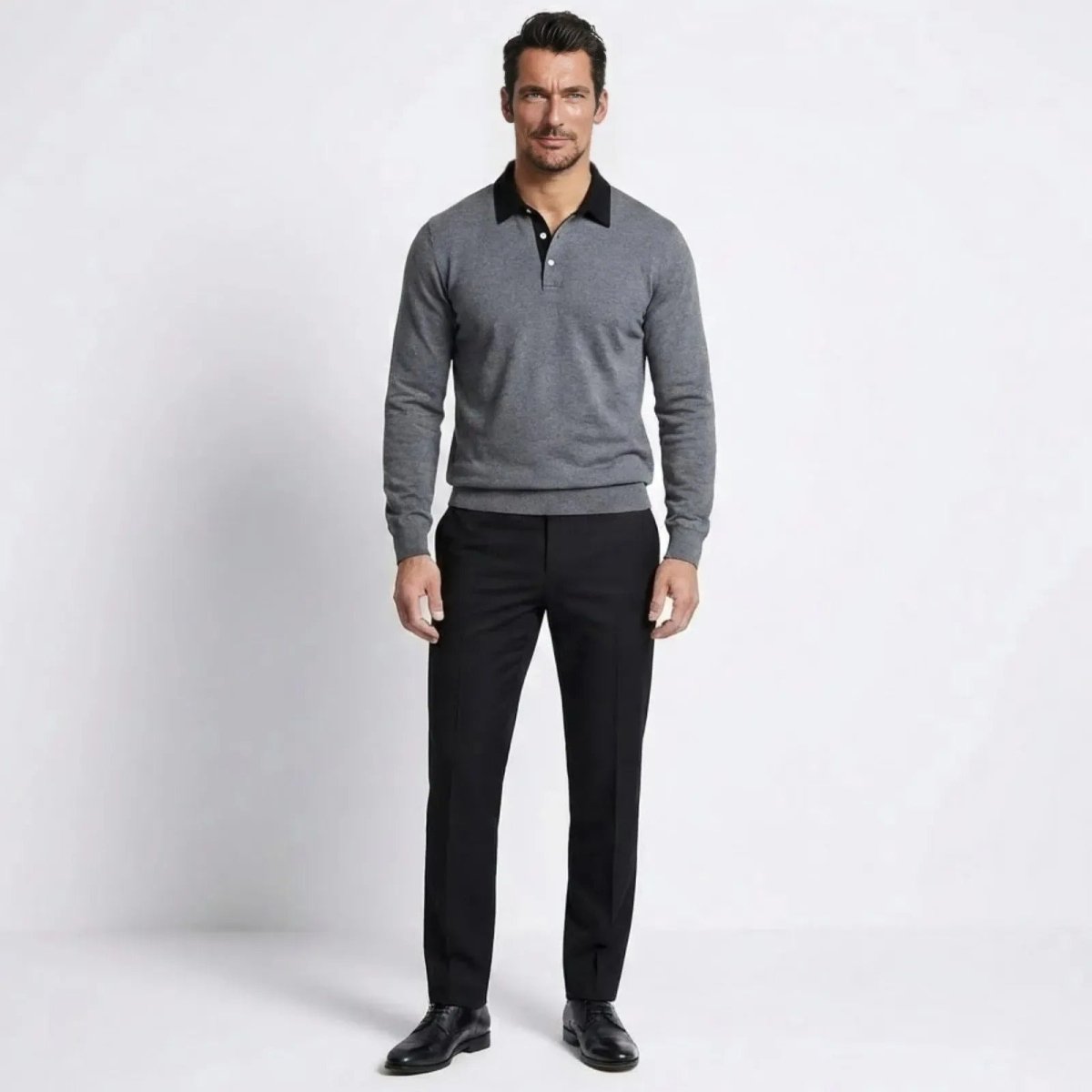 Model wearing the Kouvr men's long-sleeve merino wool polo sweater in heather dark grey with a black contrast collar, styled with black trousers.