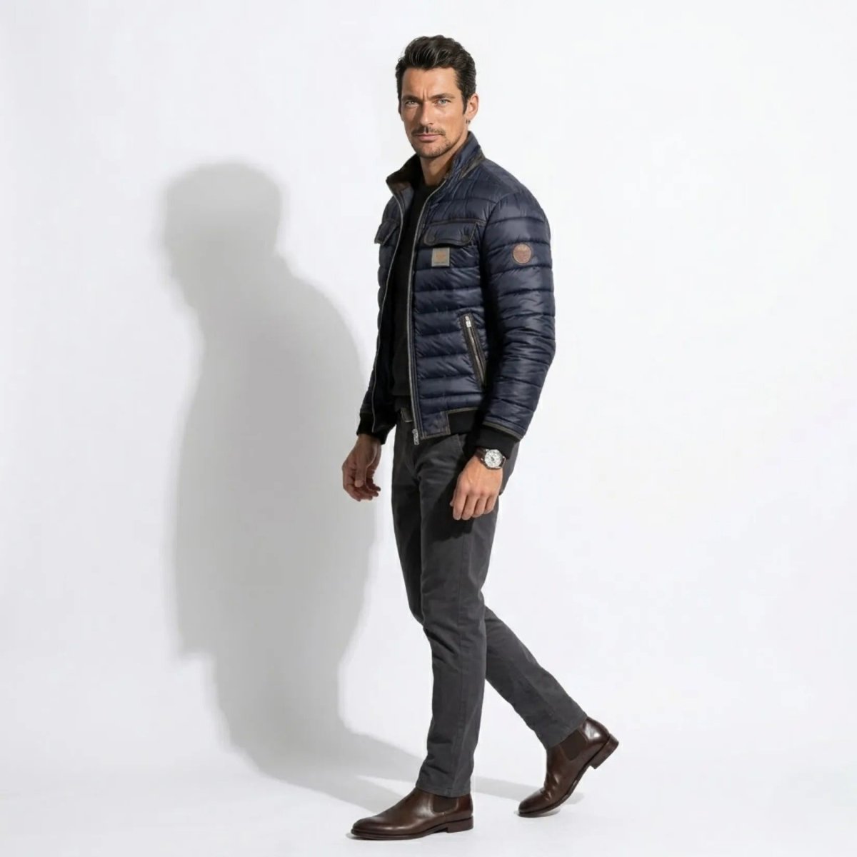 Side profile of male model walking in the Kouvr slim fit navy blue puffer coat highlighting the left arm logo patch.