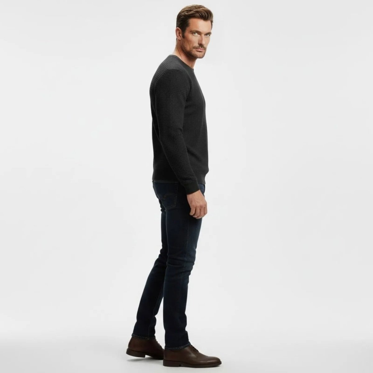 Side profile of a male model in the Kouvr black waffle-knit pullover showing the slim fit and sleeve length.