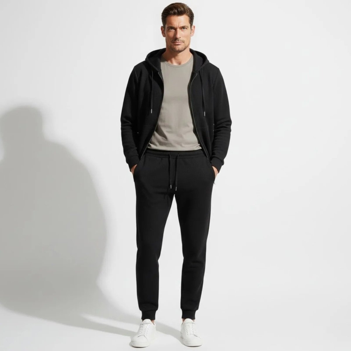 A male model wearing the Kouvr black waffle-knit tracksuit set, including a zip hoodie and matching joggers, shown from the front.