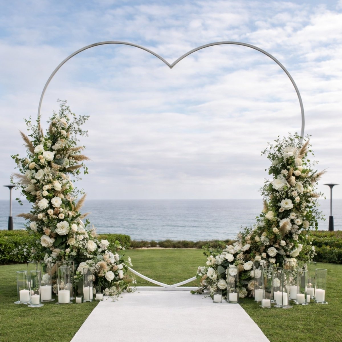 Luxury outdoor oceanfront wedding backdrop utilizing a heart-shaped frame covered in lush white roses and greenery.