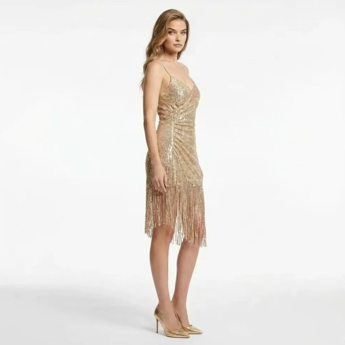 Side profile view of a woman in a champagne gold sequin cocktail dress with spaghetti straps and fringe detail by Kouvr.