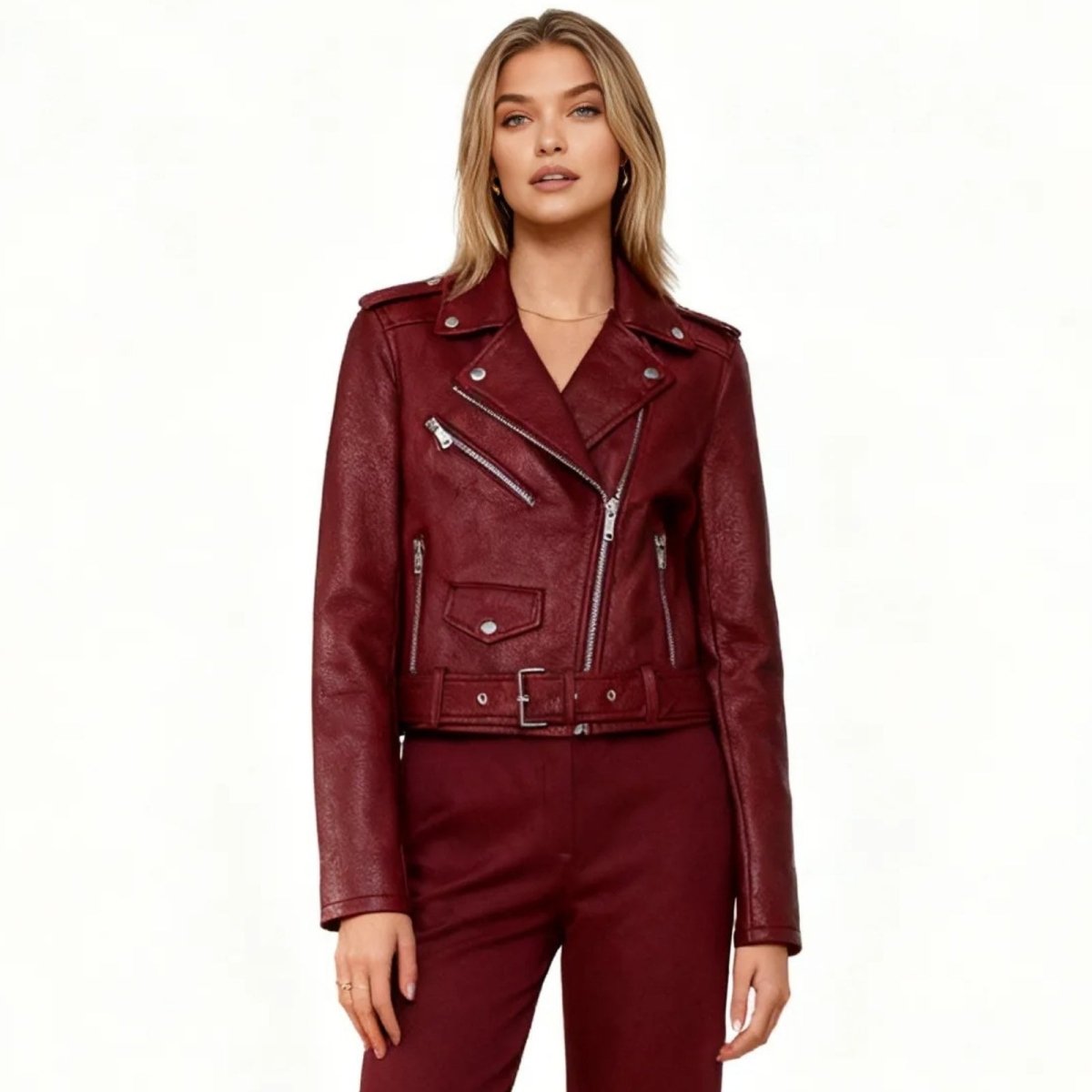 Blonde model wearing the Kouvr Reshane burgundy faux leather moto jacket with matching pants, showing the front asymmetrical zip and belted waist.