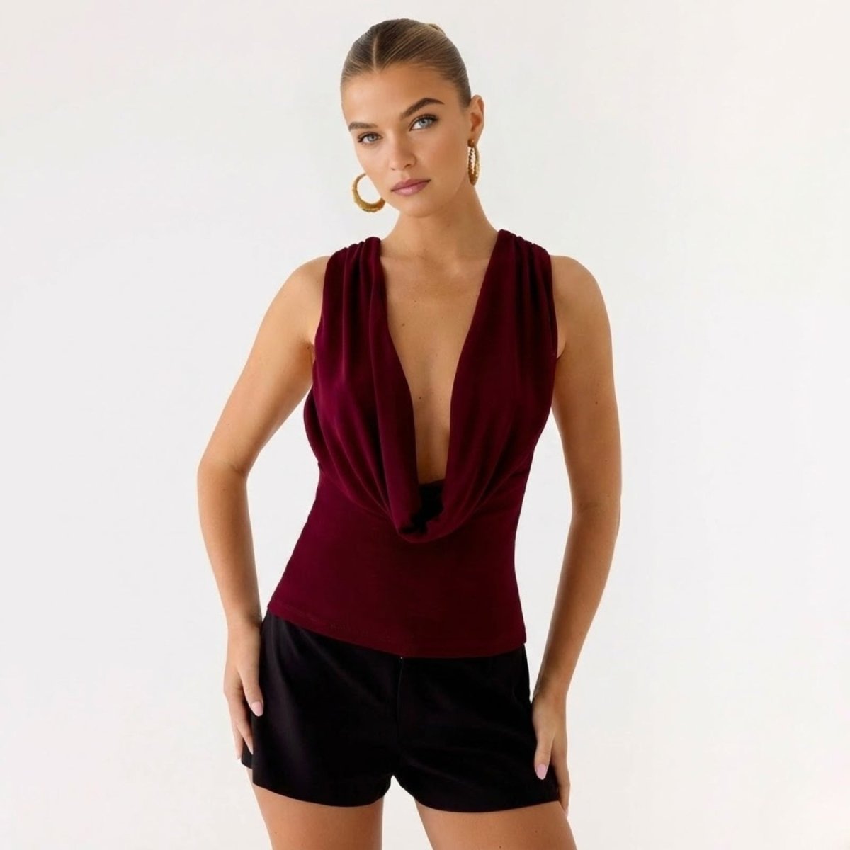 Model wearing the Kouvr Rhea top in burgundy, showcasing the deep draped cowl neckline.