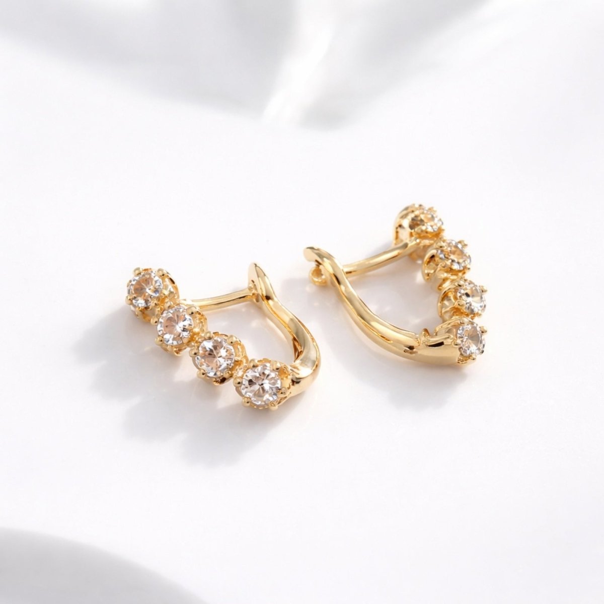 A detailed lifestyle shot of the Kouvr 14k rose gold and zircon earrings lying on a soft white surface, highlighting their sparkle.