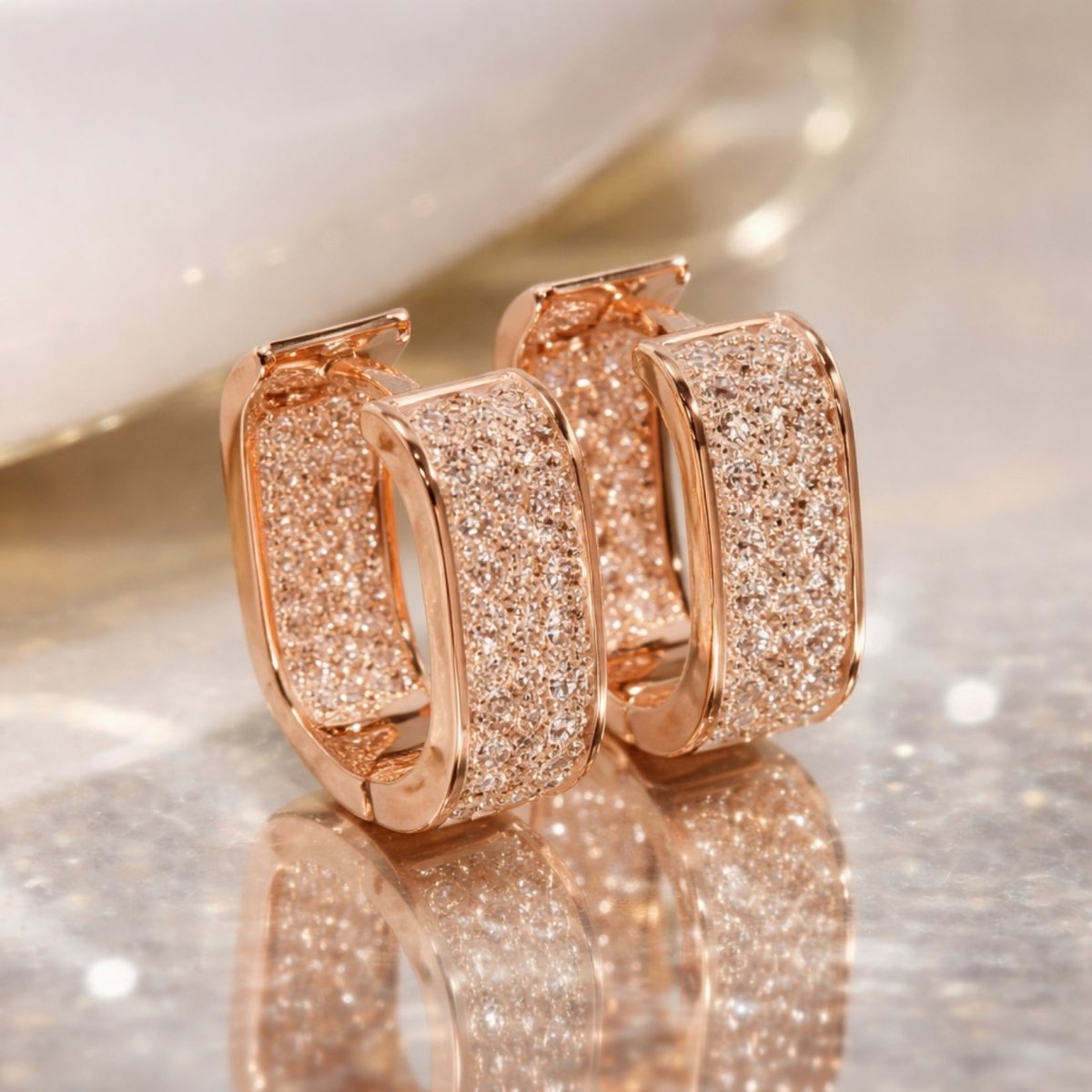 The complete Kouvr Salome U-hoop earring collection, showing two pairs in 18k gold plate and two pairs in rhodium plate (silver tone), displayed on a brown leather surface.