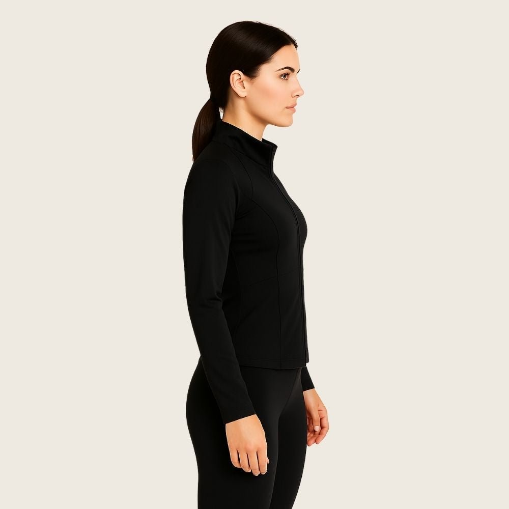 Woman wearing the black Kouvr Sculpting Athletic Jacket in a modern fitness studio.