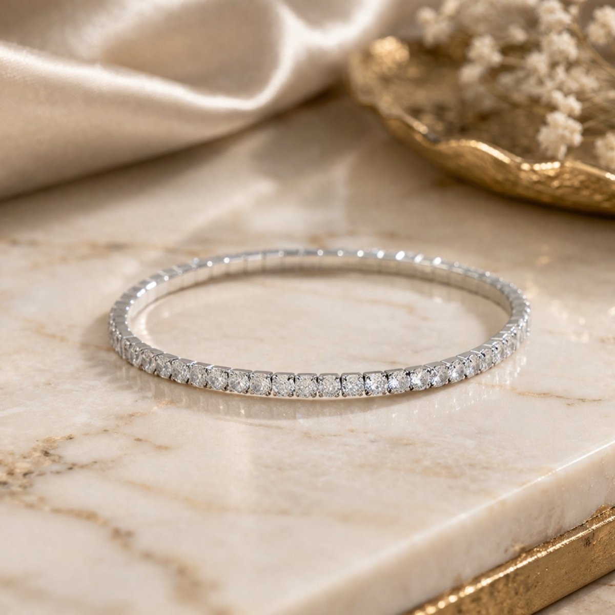 The Kouvr silver stretch tennis bracelet styled on a marble surface with silk and gold accents, highlighting its luxury quality.