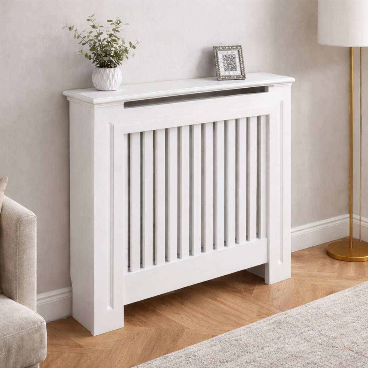 Small white slatted radiator cover with a potted plant and a picture frame, demonstrating its use as a compact shelf.