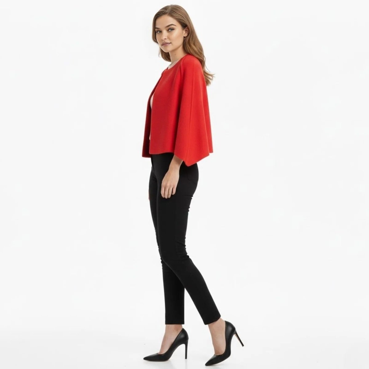 Side view of a woman walking in a cropped red collarless cape jacket by Kouvr, showing the elegant sleeve drape.