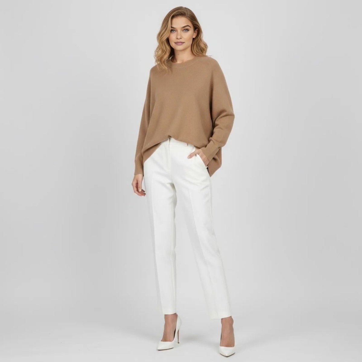 Model wearing the Kouvr Tina oversized cashmere blend sweater in light brown with white trousers, front view.