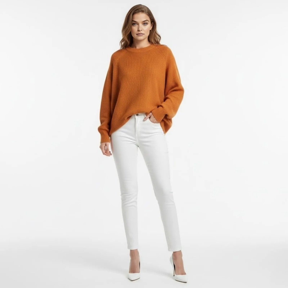 Model wearing the Kouvr Tina oversized dolman sleeve sweater in burnt orange, styled with white skinny jeans and white heels.