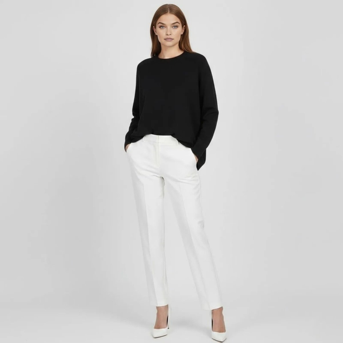 Model wearing the Kouvr Fashion Tina oversized black merino cashmere sweater with white trousers, front view.