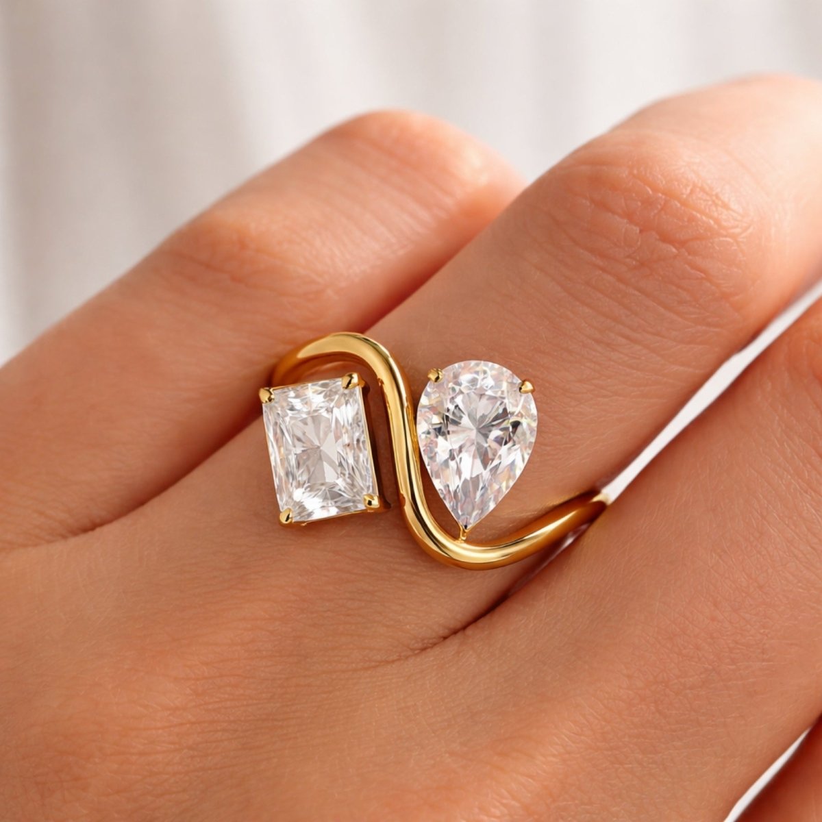 A woman's hand wearing the Kouvr Toi et Moi two-stone diamond ring, showcasing the bypass design and brilliance of the pear and princess diamonds.