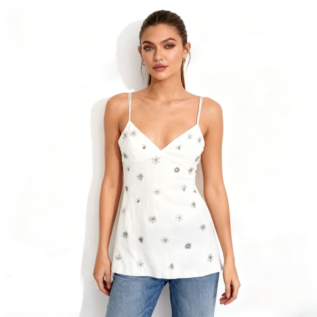 Front view of the Kouvr white beaded cami top featuring a V-neckline and scattered crystal floral embellishments on a white background.