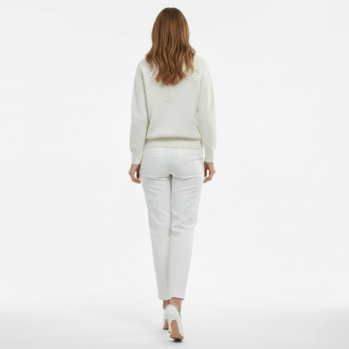 Full back view of a model in the Kouvr white knit sweater, showing floral appliqué detail on the shoulders.
