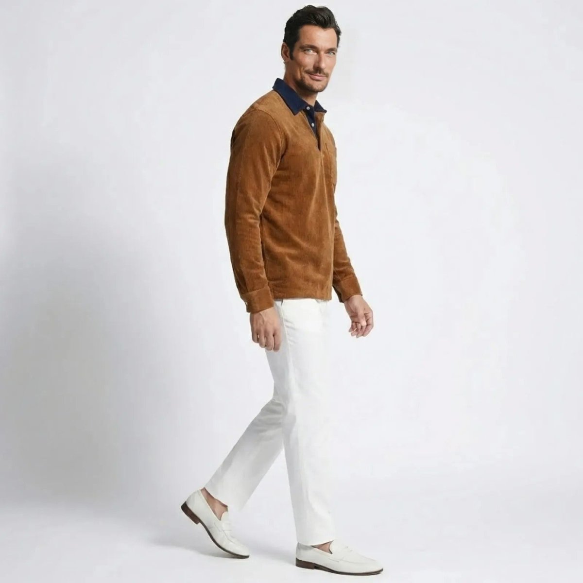 Side profile of a man walking in a orange corduroy long sleeve polo shirt and white pants, showcasing its fit and texture.