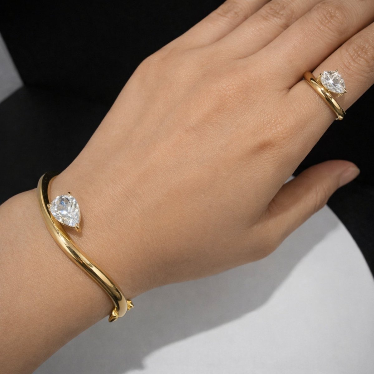 A woman's hand wearing the matching Kouvr Zella ring and bypass bangle bracelet set in 18k gold with pear cut stones.