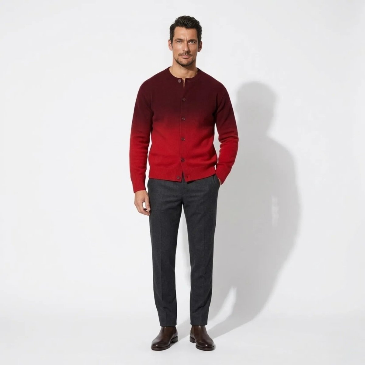 Male model wearing Kouvr men's burgundy to red ombre gradient knit cardigan sweater with dark trousers and brown chelsea boots.